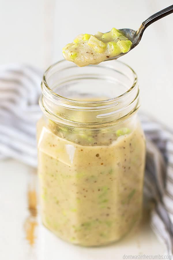 A glass jar with cream of celery soup and a spoon with some of the soup on it.