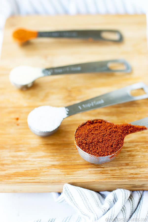 Spices in different measuring spoons on top of a wooden cutting board