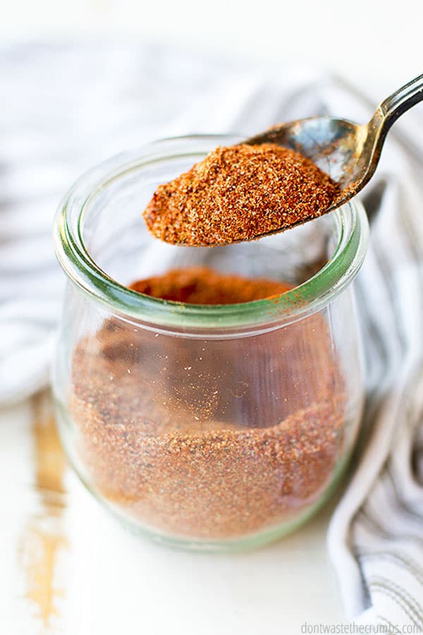 Chili seasoning in a small glass jar with a spoonful of seasoning