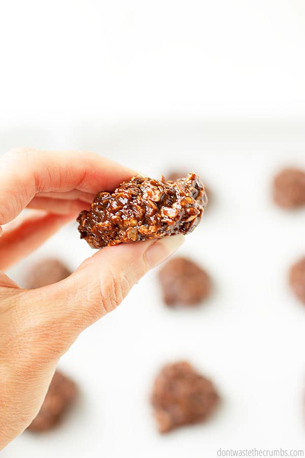 A hand holding a delightfully chocolate and oat filled no bake cookie in front of a blurred background containing other cookies. 