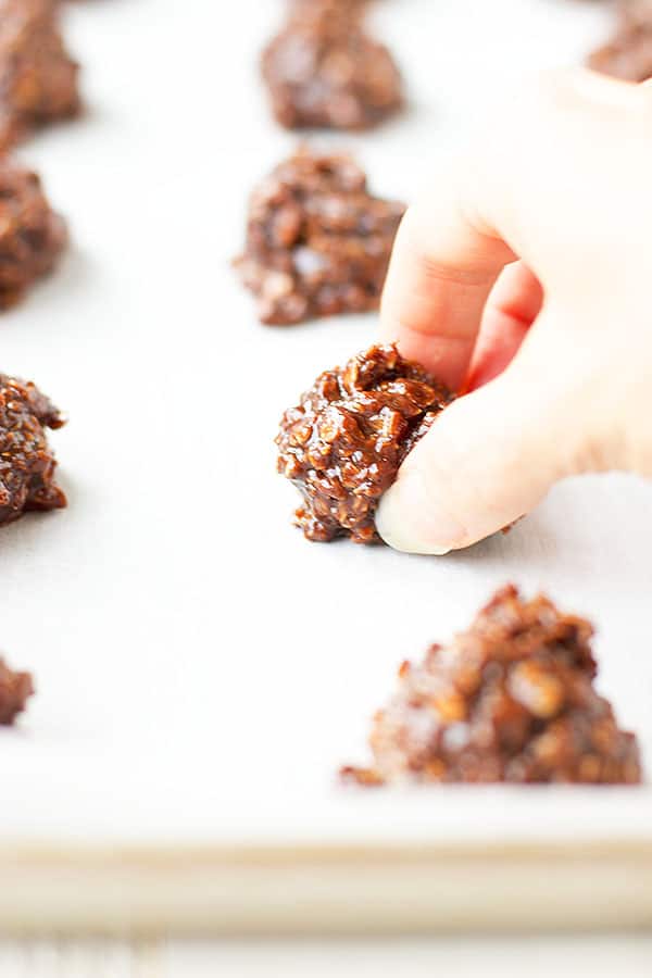 A hand reaching out to grab a single no bake cookie from a cookie sheet with rows of my No Bake Cookies. 