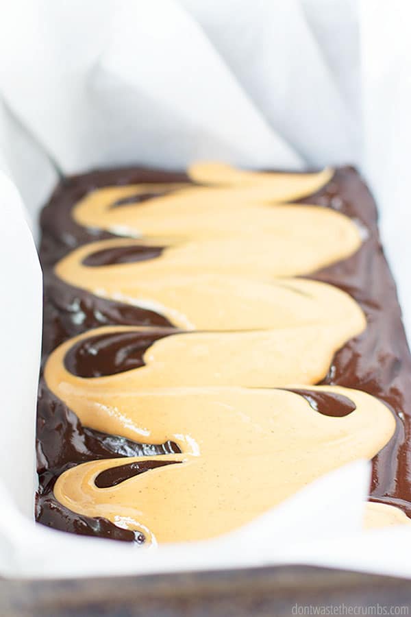 Melted chocolate and condensed milk in a lined large loaf pan with creamy peanut butter swirled on top.