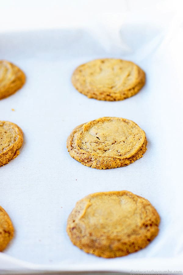 Three whole  cookies and three cookie edges on a parchment sheet. They are golden brown and delicious.