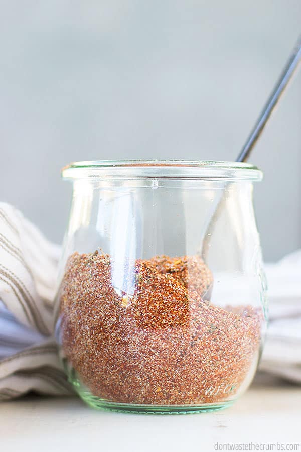 Homemade Cajun seasoning in a glass spice jar with a spoon in it.