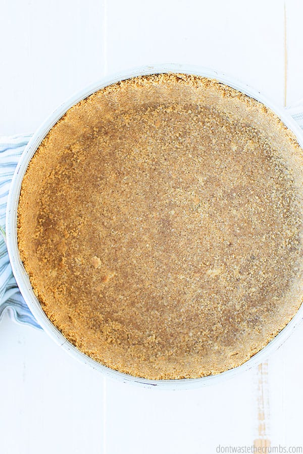 A moist and crumbly graham cracker crust is sat upon a white wooden table and a towel.