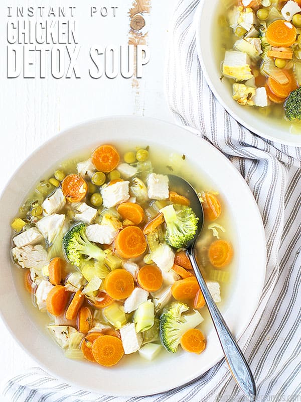 The cover photo of our Instant Pot Chicken Detox Soup. Two bowls of delicious soup sit upon a white wooden table and next to a towel.