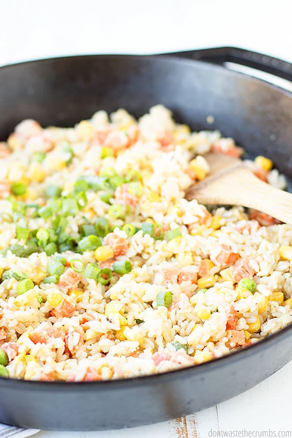 Vegetable fried rice in a cast iron skillet topped with green onions and being mixed with a wooden spoon.