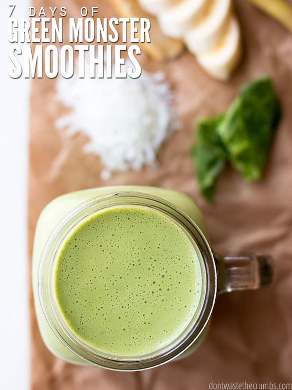 Bird's eye view of a green smoothie in a large glass cup. Spinach and sliced bananas are in the background. Text overlay reads, "7 Days of Green Monster Smoothies".