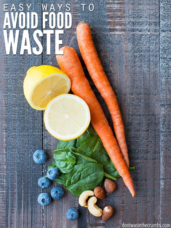 Two bright orange carrots, a sliced lemon, a pile of spinach, six blueberries, and a handful of nuts. The text overlay says "Easy Ways to Avoid Food Waste"