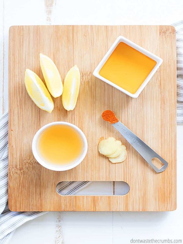 Apple cider vinegar, lemon juice, ginger, raw honey, and cayenne. All the ingredients are laid out on a cutting board in preparation for this healthy elixir.