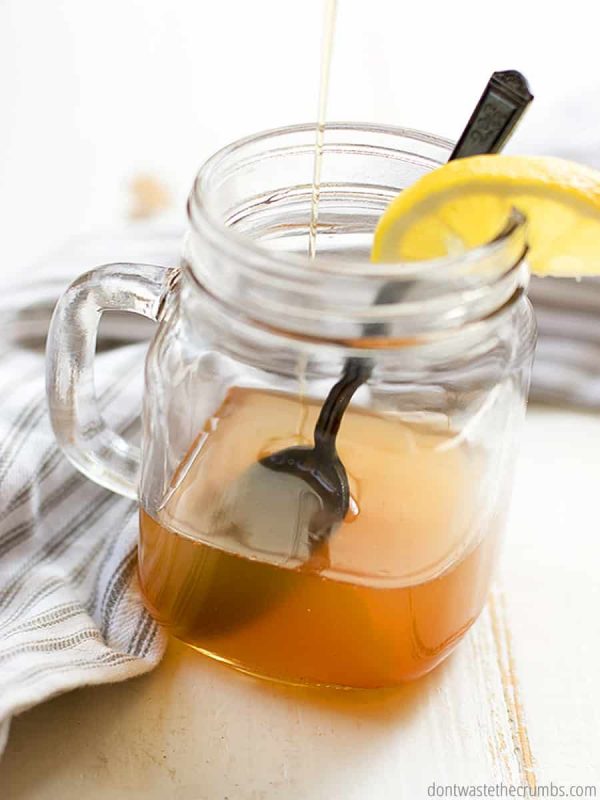 Apple cider vinegar detox drink in a glass mason jar cup with a spoon in it and sliced lemon wedge on the brim