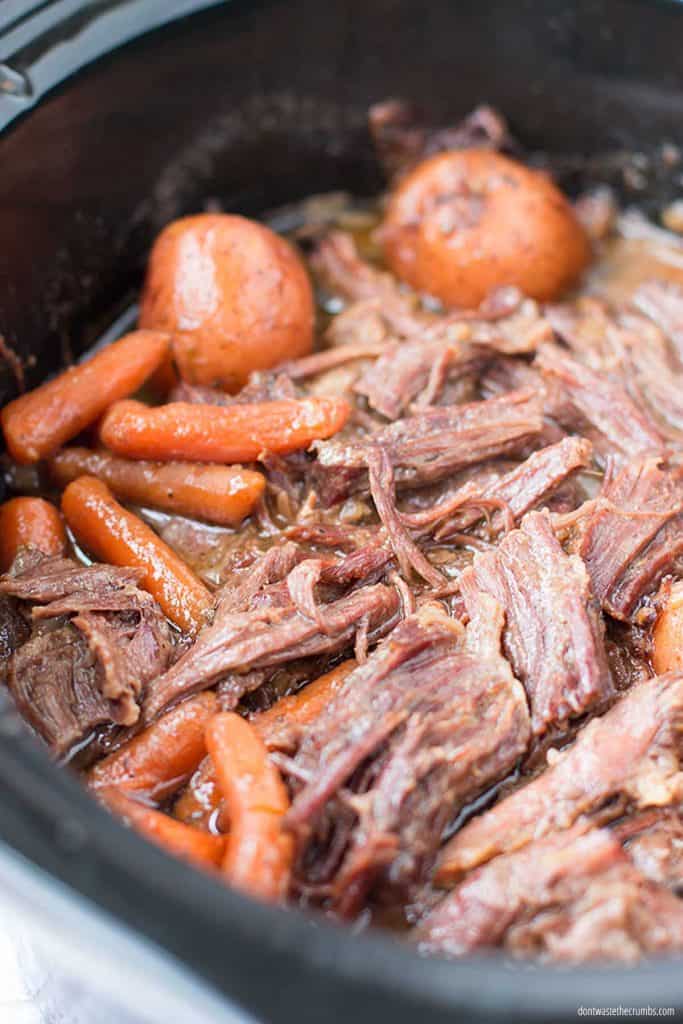 This delicious slow cooker pot roast is paired with potatoes, carrots, and dry onion mix inside of a black oval slow cooker.  
