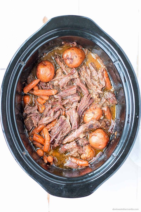 Oval slow cooker with cooked homemade pot roast in it.