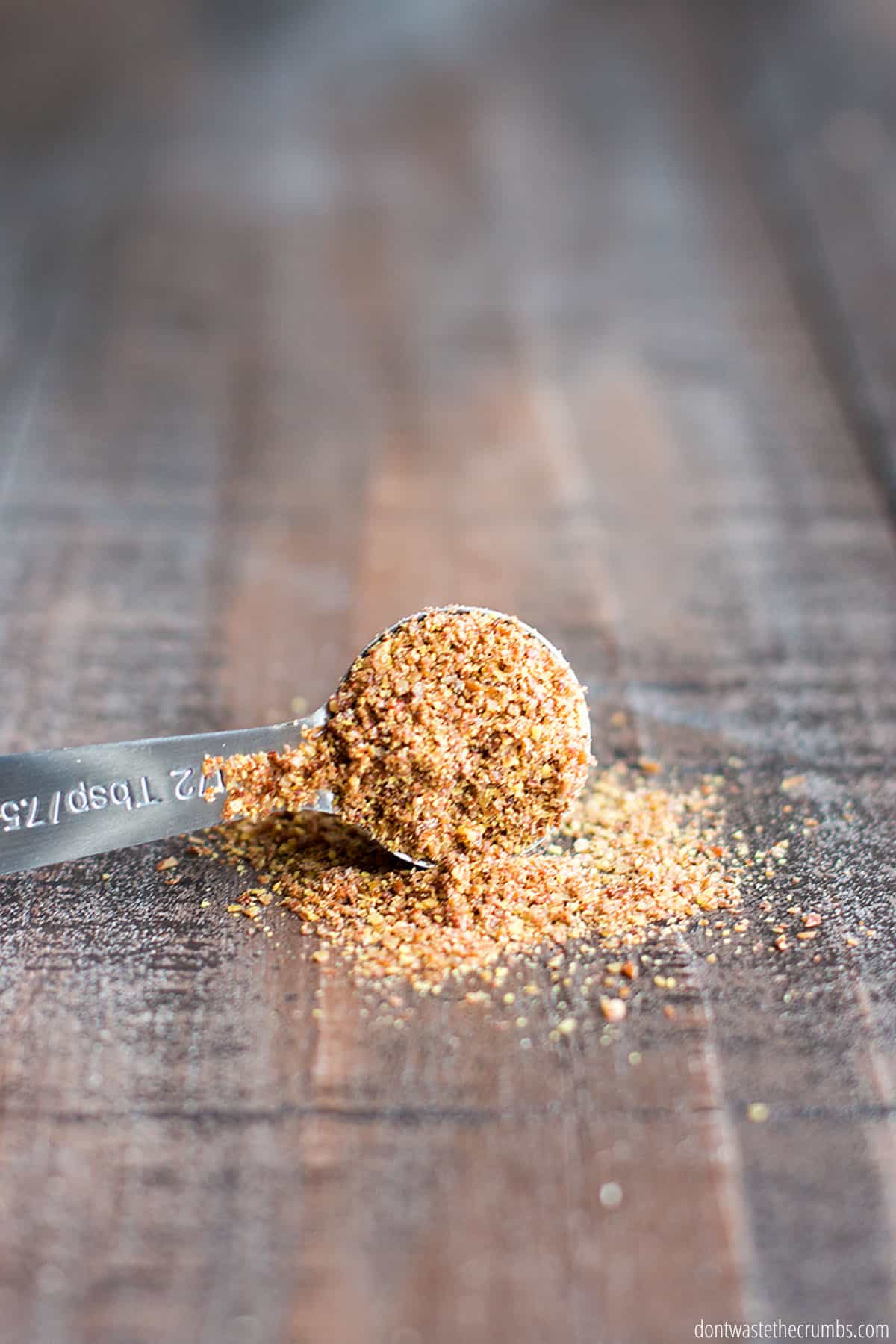 A 1/2 Tbsp full of flaxseed meal is laying on it's side with some flaxseed spilled out onto the table.