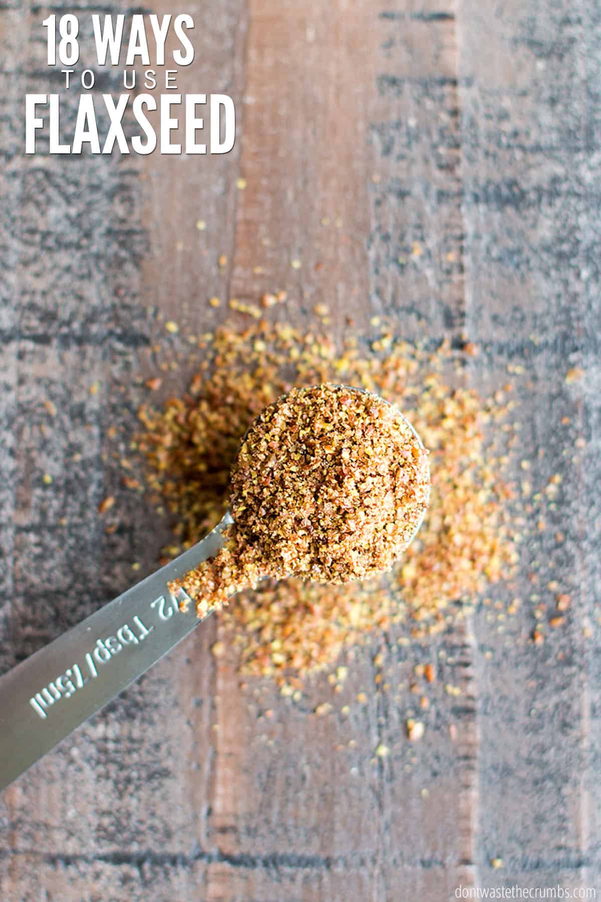 A stainless steel measuring spoon heaping full of milled flaxseeds. Some of the flaxseed meal is spilled over onto the table. The text overlay reads, "18 Ways to Use Flaxseeds."