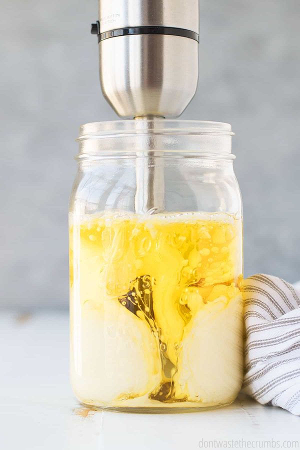 Immersion blender mixing in a large mason jar with olive oil and egg in it