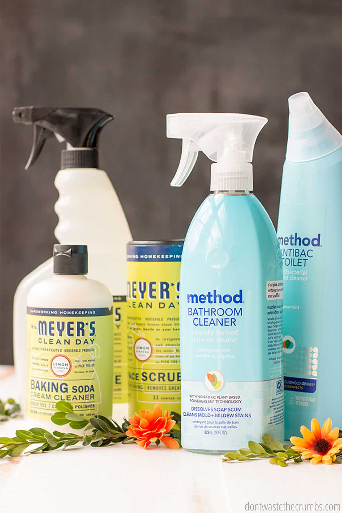 Pictured are five products that can be purchased at Grove Collaborative. A bathroom cleaner, baking soda cream cleaner, scrub cleaner and toilet cleaner. Flowers are placed on the table beside the cleaning products.