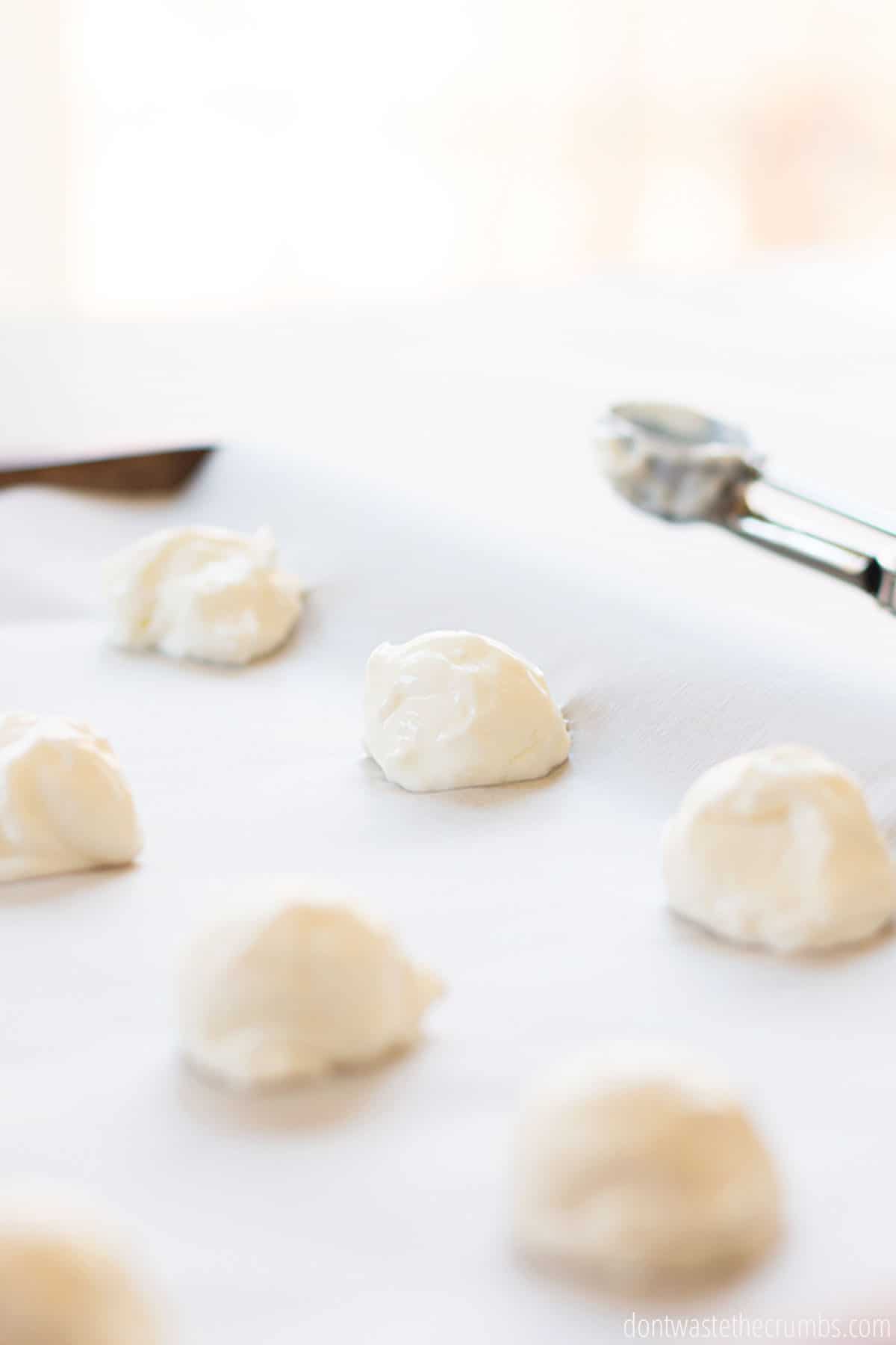 Six small scoops of yogurt on parchment paper on a baking sheet. The scooper can be seen in the background.