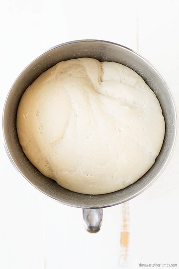 A metal mixing bowl is filled with risen bread dough ready for the oven or freezer.