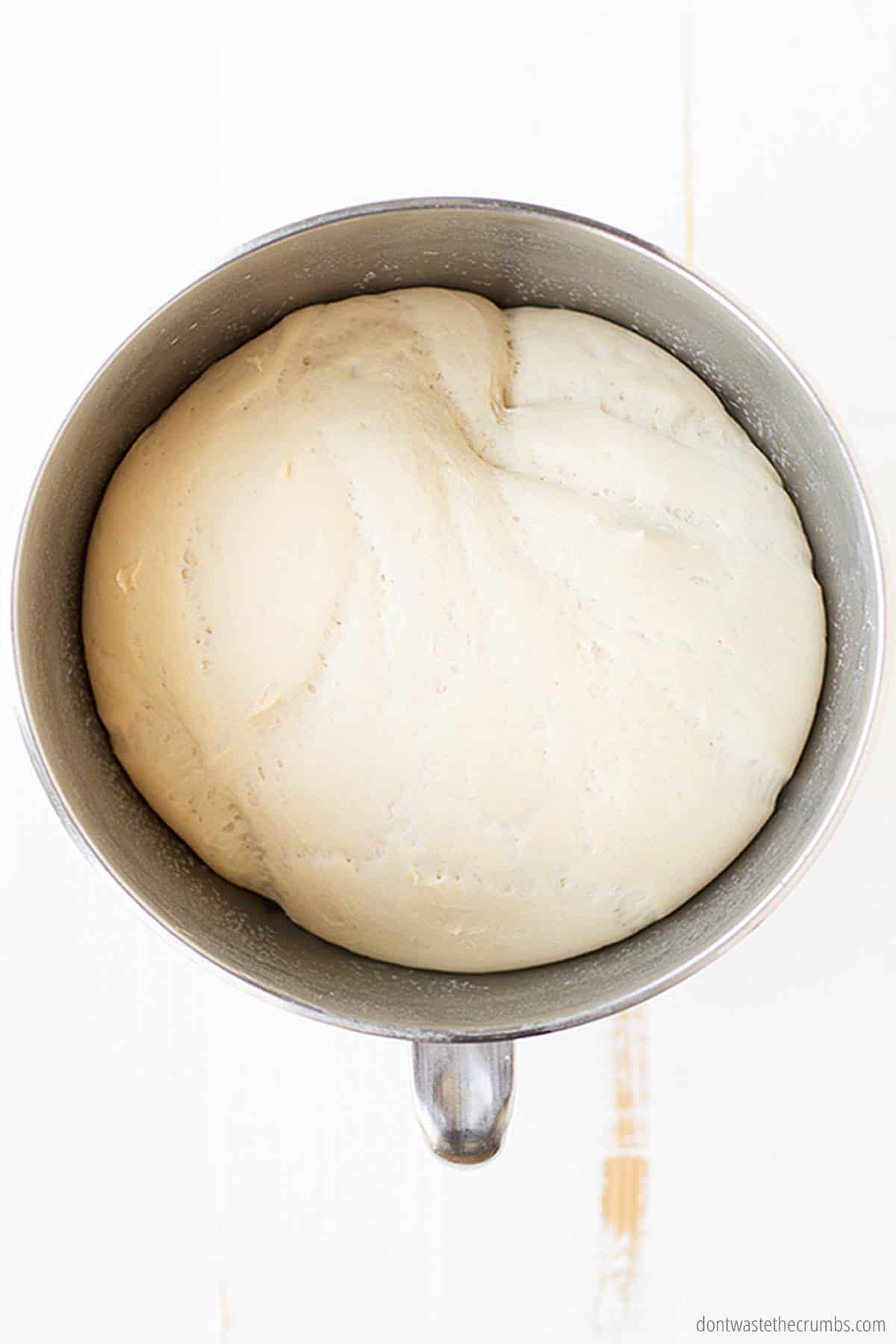 A metal mixing bowl is filled with risen bread dough ready for the oven or freezer.
