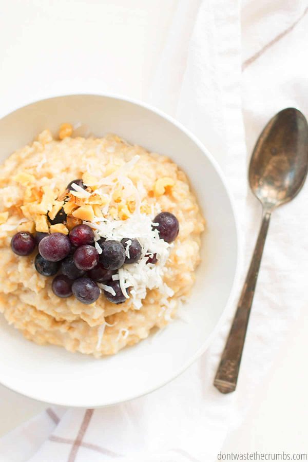 Bowl of instant pot oatmeal with fresh blueberries, shredded coconut, and nuts. A spoon is nearby.