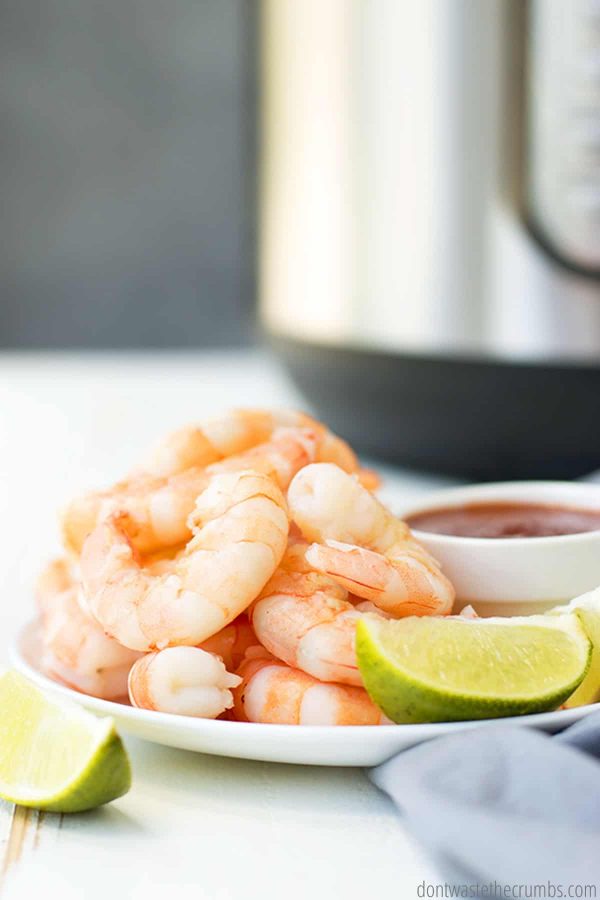 Plate of steamed shrimp with dipping sauce and slices of lime
