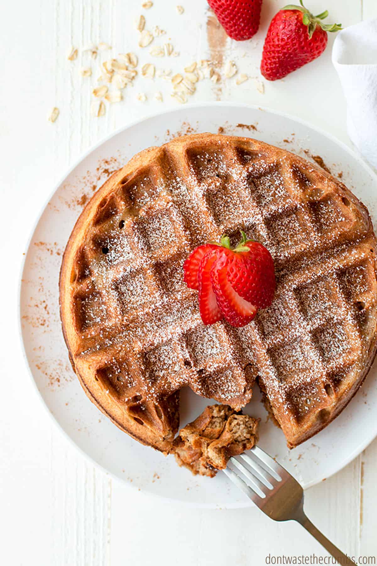 A round golden brown Belgian waffle topped with powdered sugar and sliced strawberries.