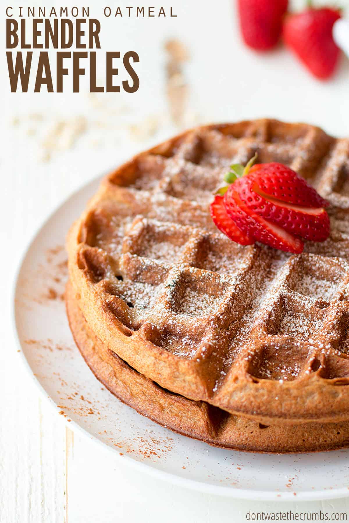 Two golden brown waffles stacked on top of a white plate. The waffles are dusted with powdered sugar and sliced strawberries. The text overlay reads "Cinnamon Oatmeal Blender Waffles."