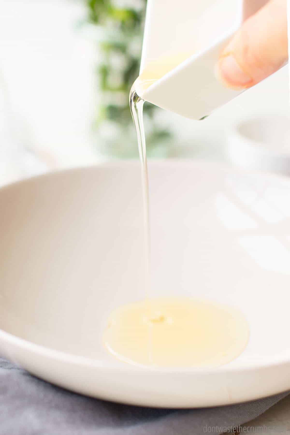 A small dish of Castile soap and vitamin E oil being poured into a larger bowl to be mixed with essential oil to make homemade foaming hand soap. 