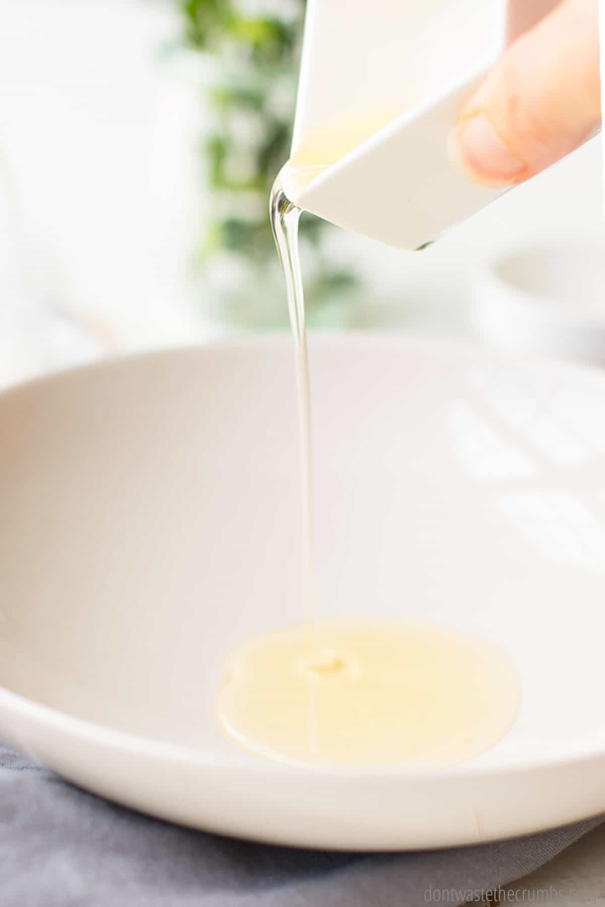 A small dish of Castile soap and vitamin E oil being poured into a larger bowl to be mixed with essential oil to make homemade foaming hand soap.