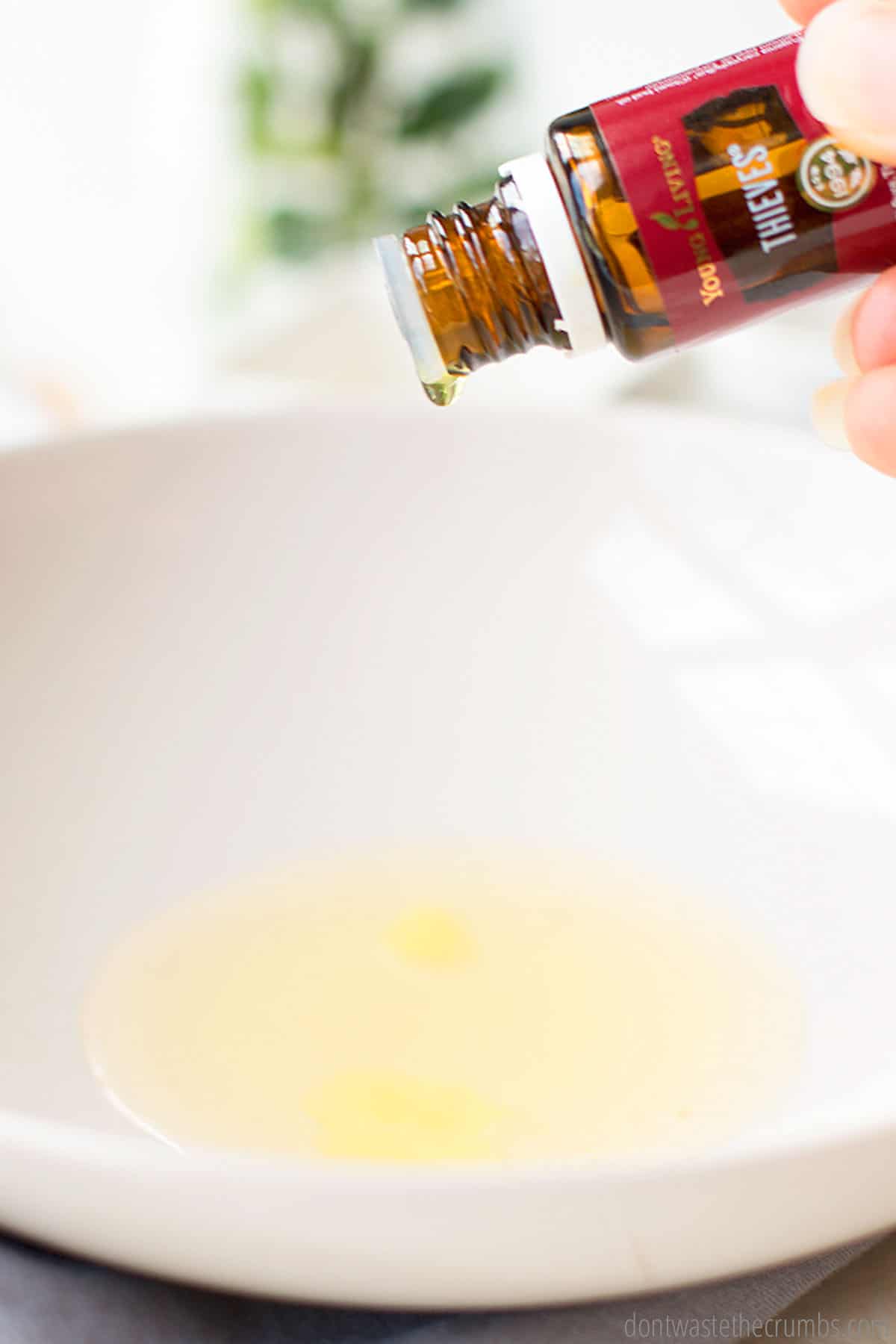 A few drops of Thieves essential oil being dripped into a large bowl with castile soap and vitamin E oil in it.