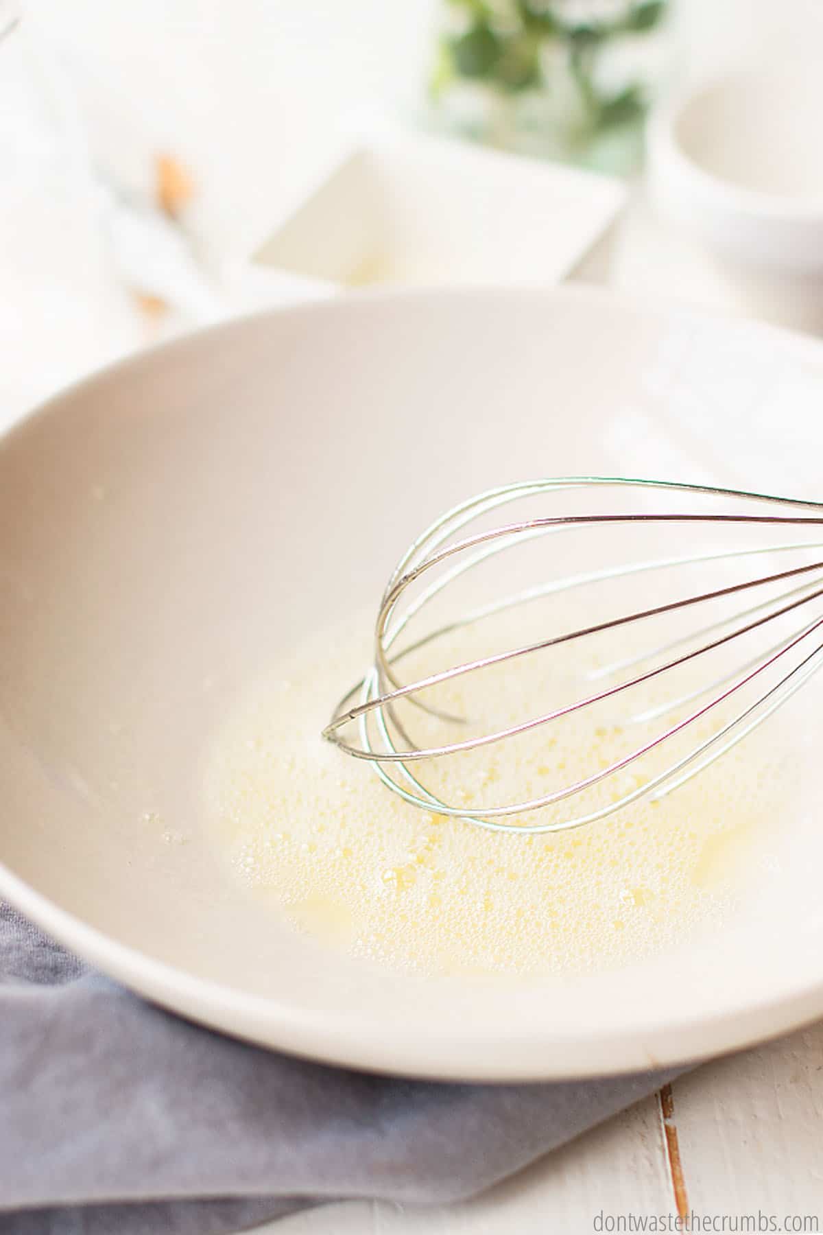 A whisk mixes castile soap, essential oils and aloe vera in a large white bowl to make foaming hand soap.