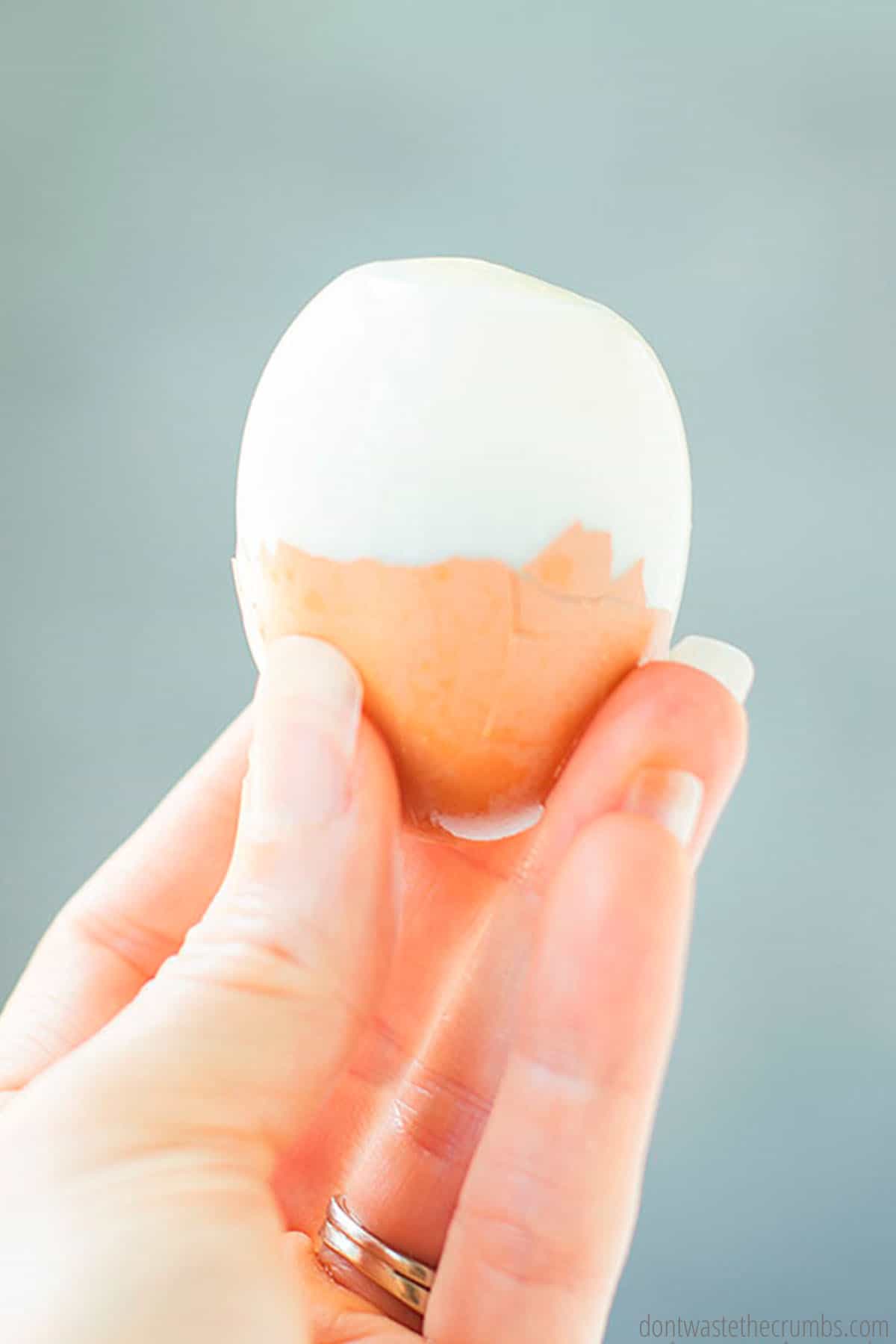 Hand holding an egg with half its peel removed.