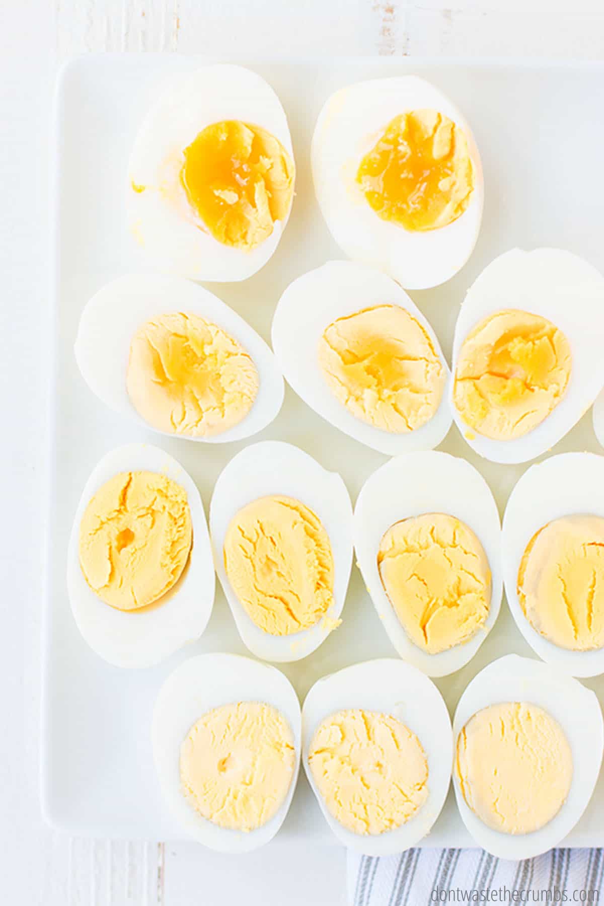 Boiled eggs, ranging from runny, soft-boiled eggs, to fully hard-boiled eggs, are displayed on a white tray.