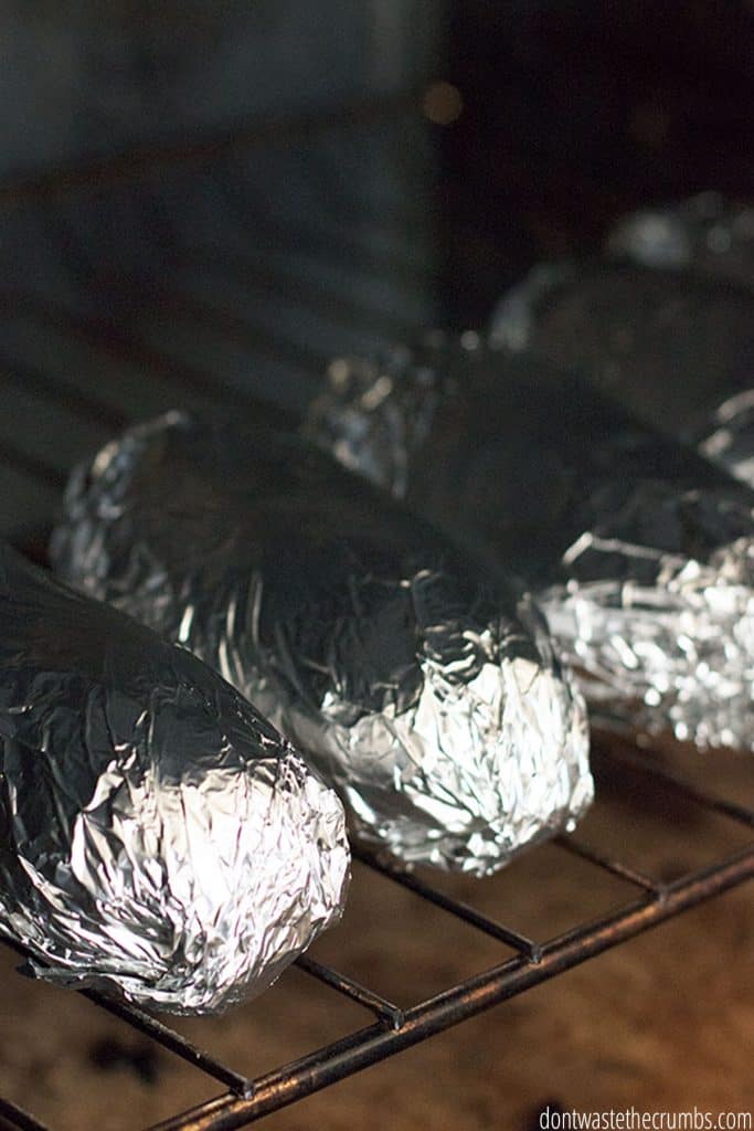 Four potatoes wrapped in foil and placed on the oven rack for baking. 