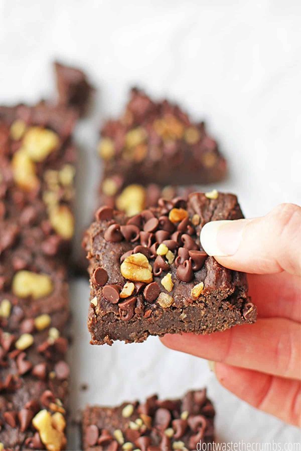 Hand holding a sliced chocolate chip black bean brownies with walnuts as a topping.
