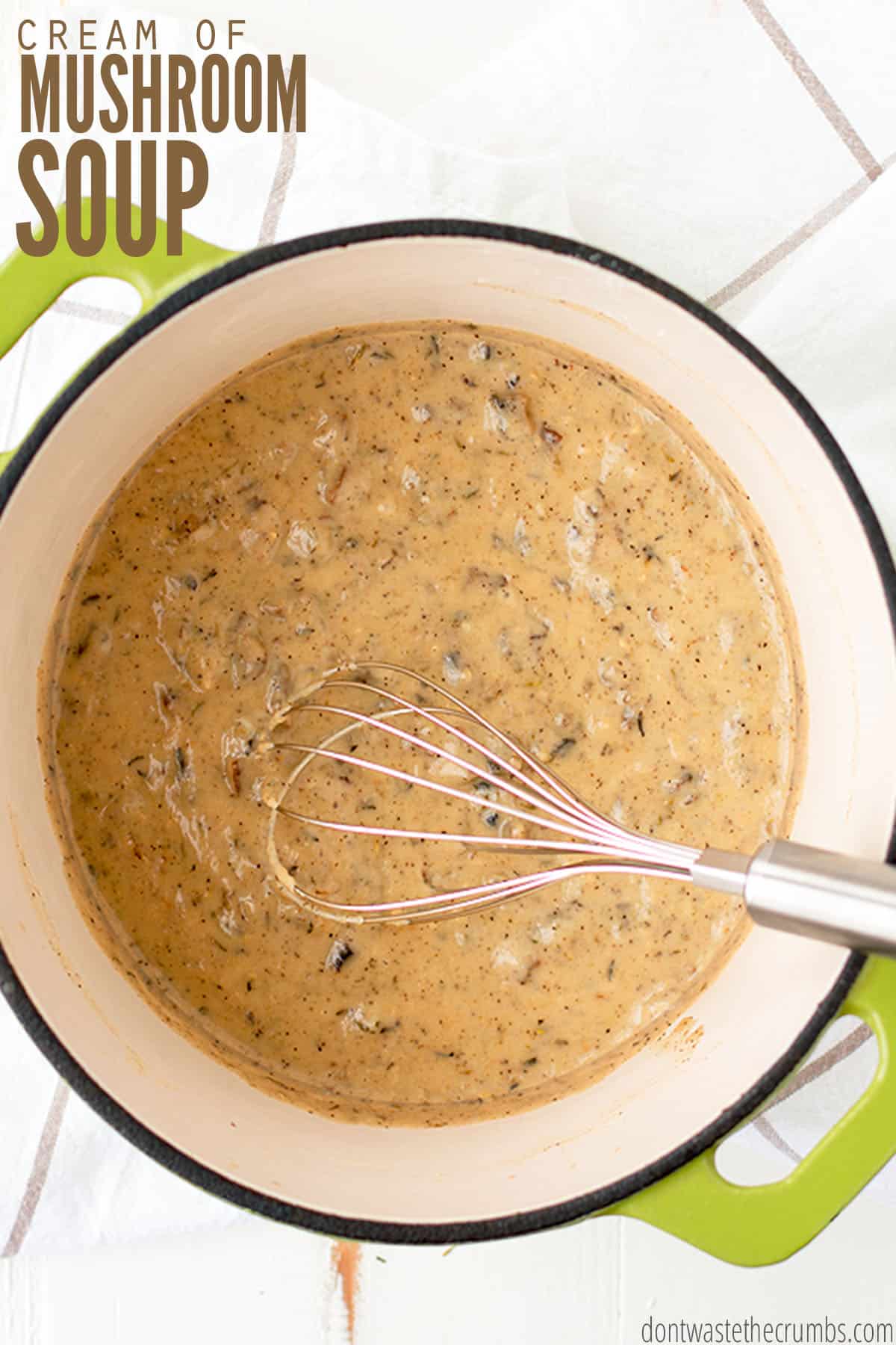 A fresh pot of homemade cream of mushroom soup inside of a dutch oven pot with a whisk inside. The text overlay reads "Cream of Mushroom Soup."