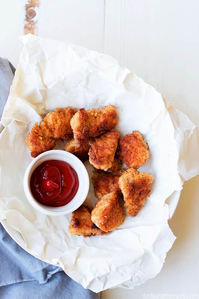 A plate is filled with brown, crispy chicken nuggets and served with ketchup.