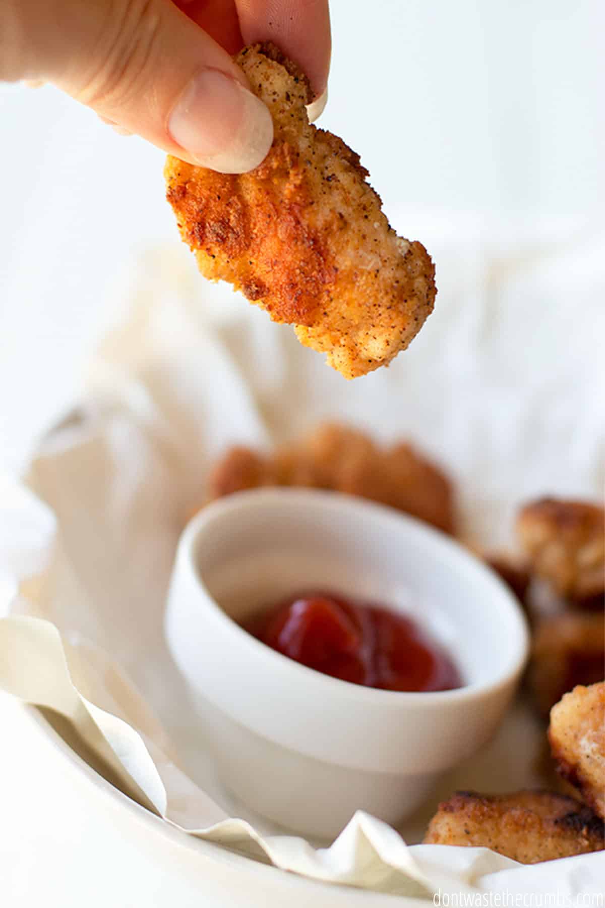 A crispy nugget hovers above a small dish of homemade barbecue sauce.