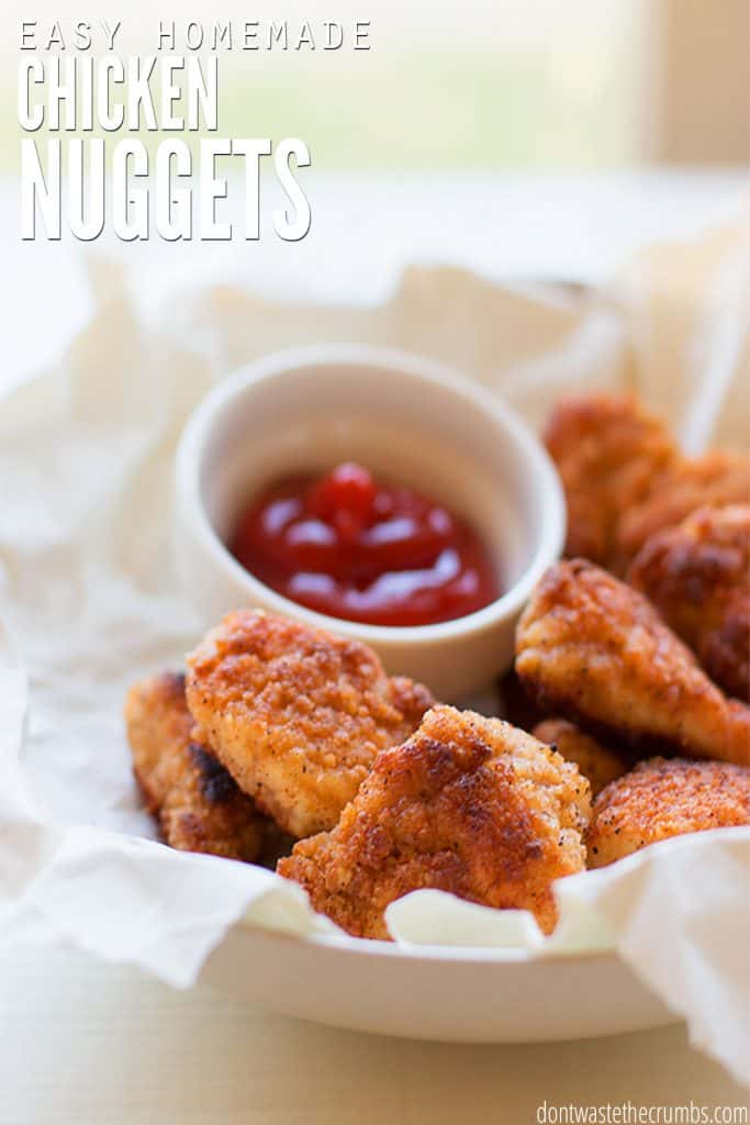 Crispy, browned chicken nuggets sit on a plate next to a cup of ketchup. Text overlay reads "Easy Homemade Chicken Nuggets."
