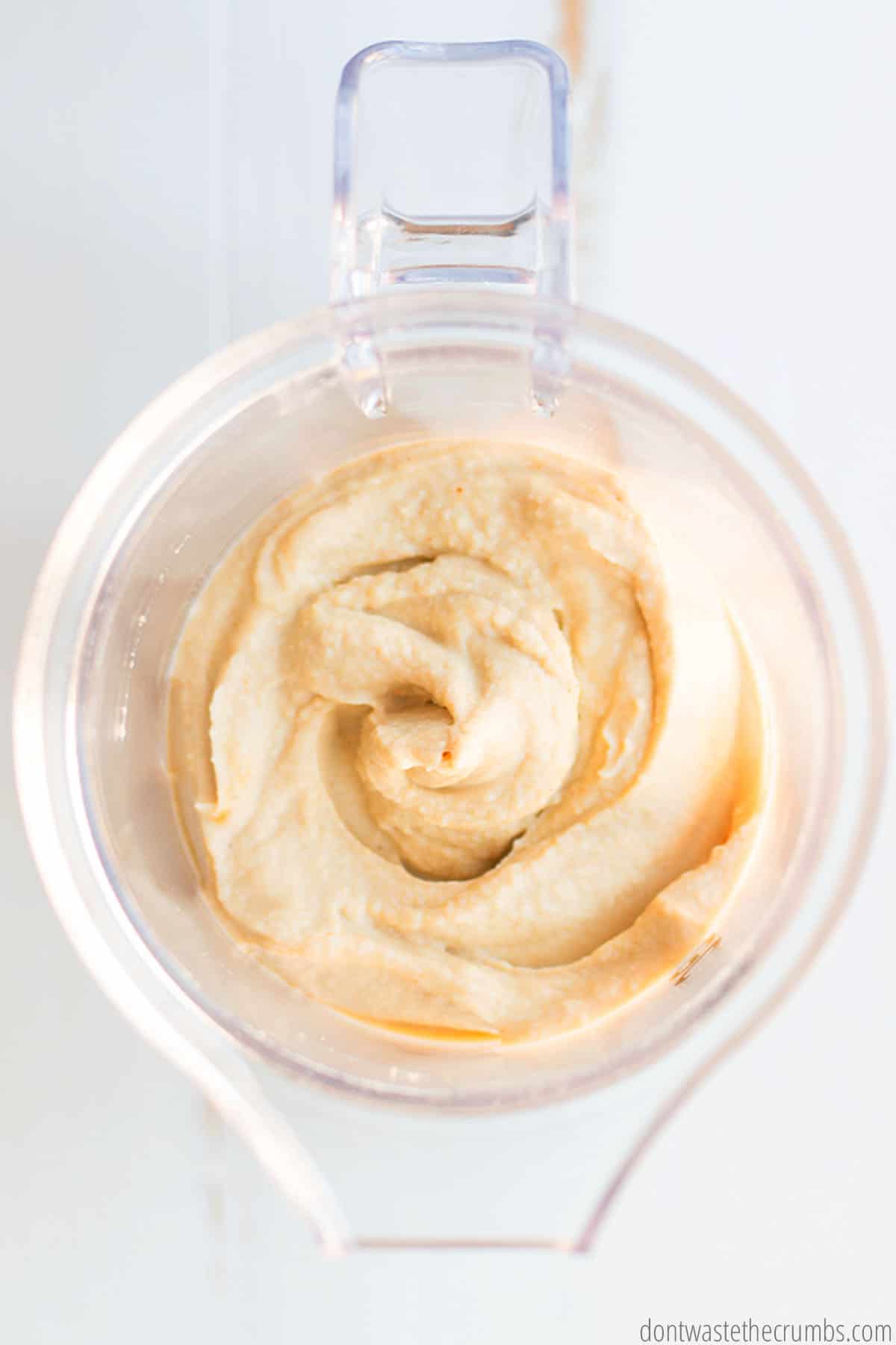 A small food processor with a freshly processed batch of traditional hummus inside.
