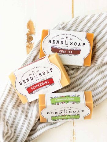 Goat milk soap benefits your skin. Bend Soap is the company that I always choose. Three bars from the company are laid out on a cloth.