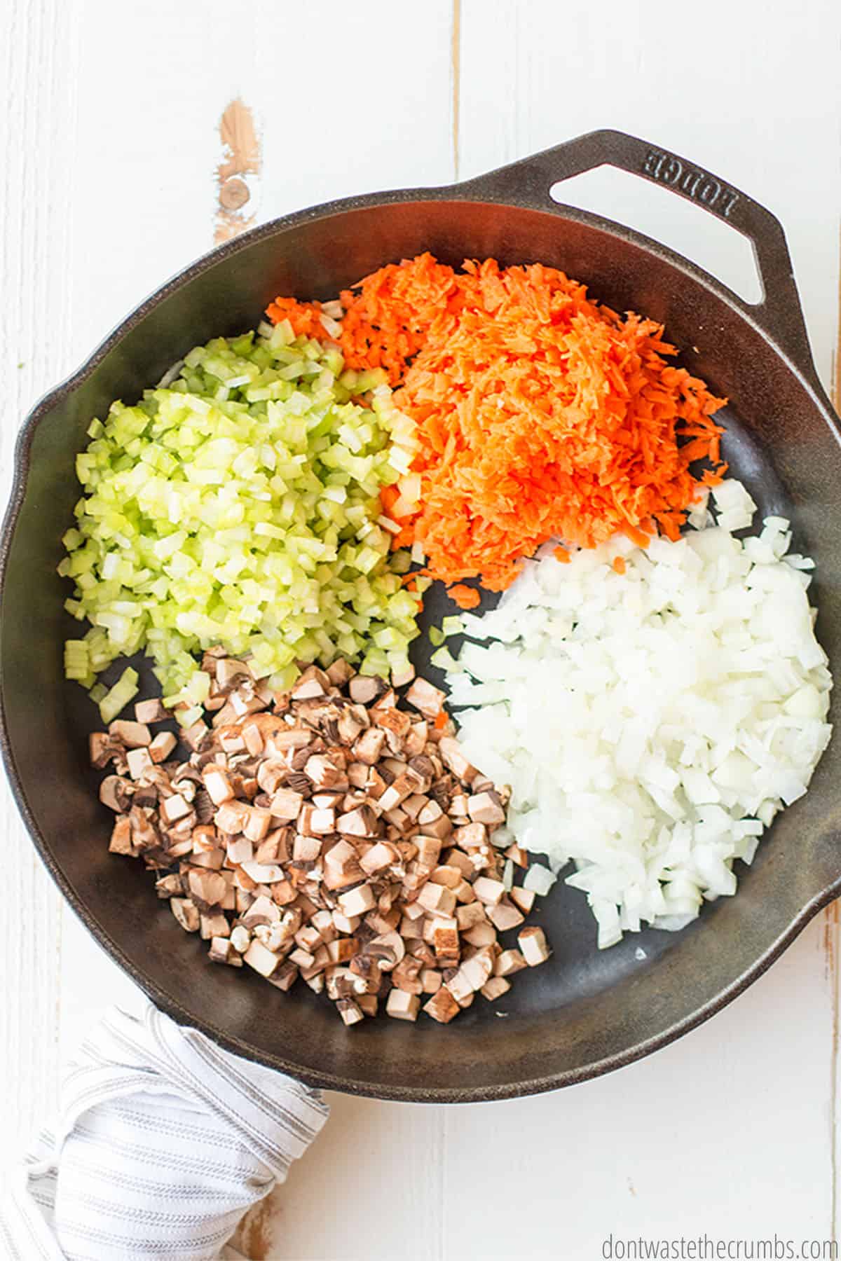 Finely chopped peppers, mushrooms, and onions, as well as shredded carrots, sit in a cast iron skillet.