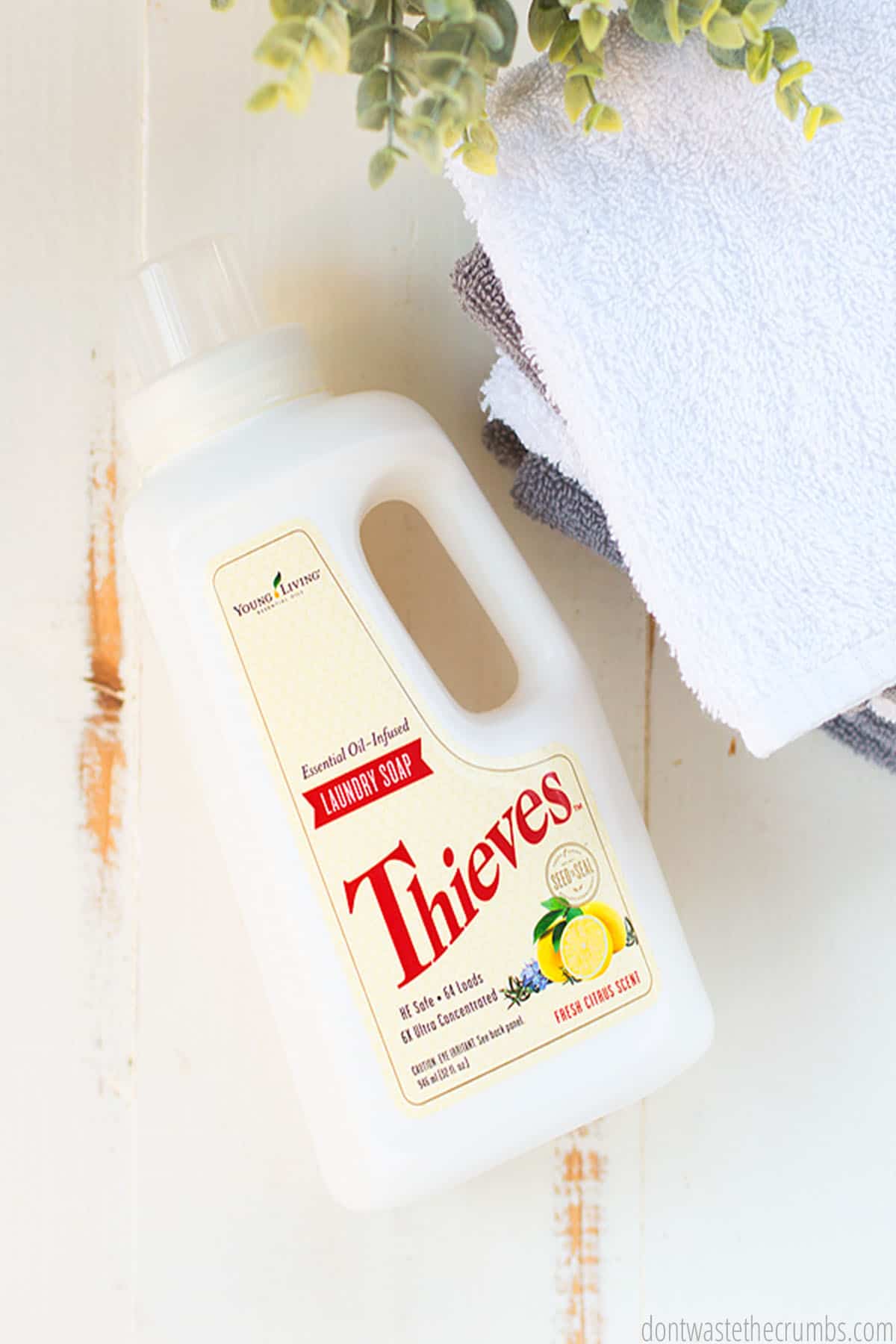 A bottle of Thieves Laundry Soap sits next to a stack of folded towels.