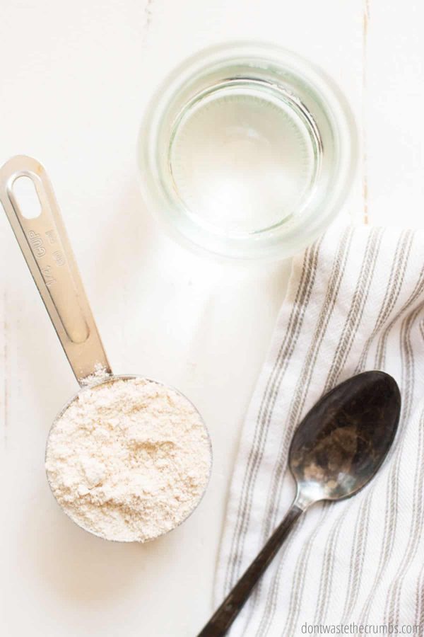 Ingredients for sourdough starter.. Flour in a measuring scoop, water in a glass, and a stainless steel spoon.