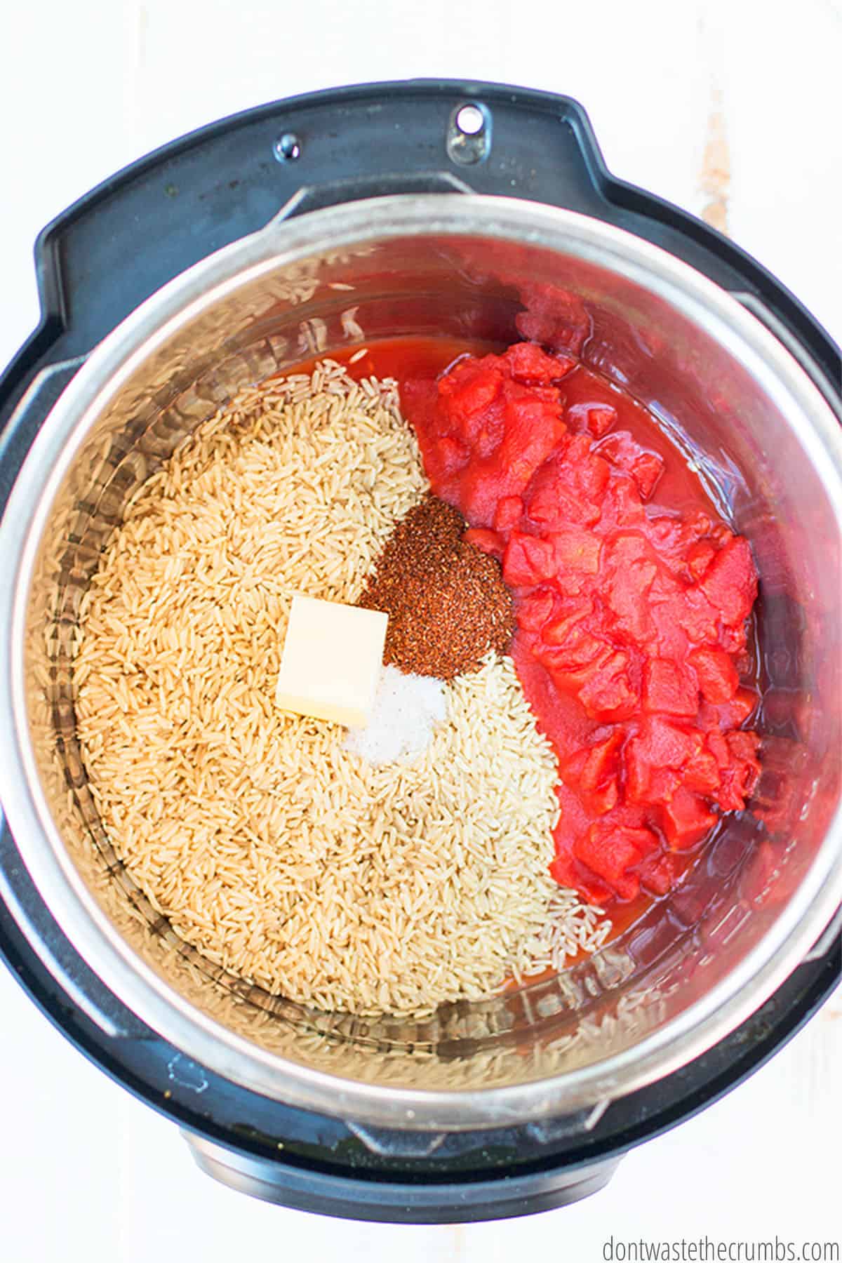 An Instant Pot is filled with uncooked rice, spices, diced tomatoes, and a chunk of butter.