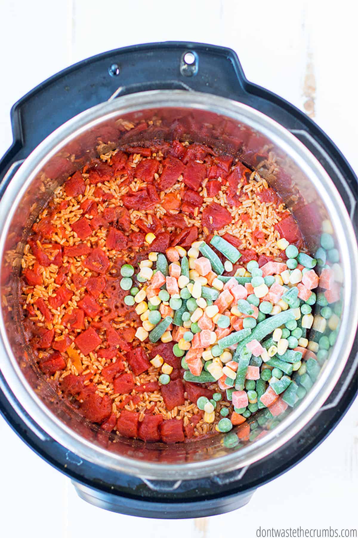 Frozen vegetables are added to the cooked rice in the Instant Pot.