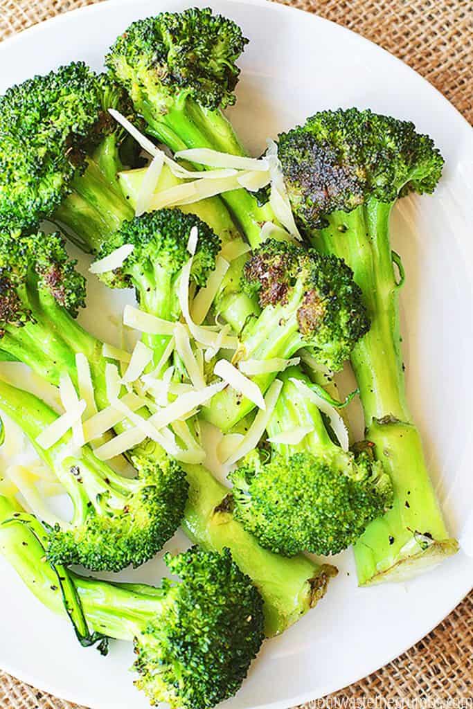 Pan-roasted broccoli is served on a white plate and garnished with shredded parmesan cheese.