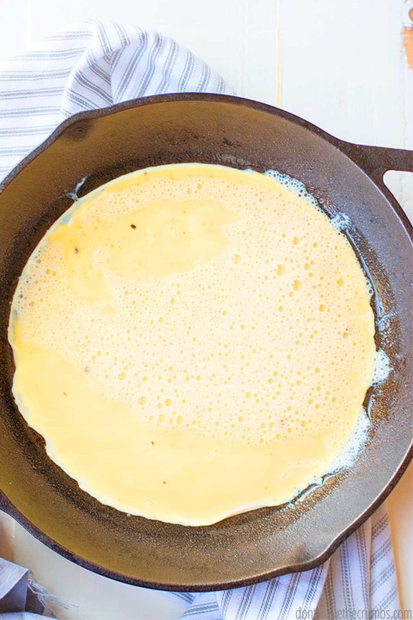 Raw eggs in a cast iron skillet cooking.