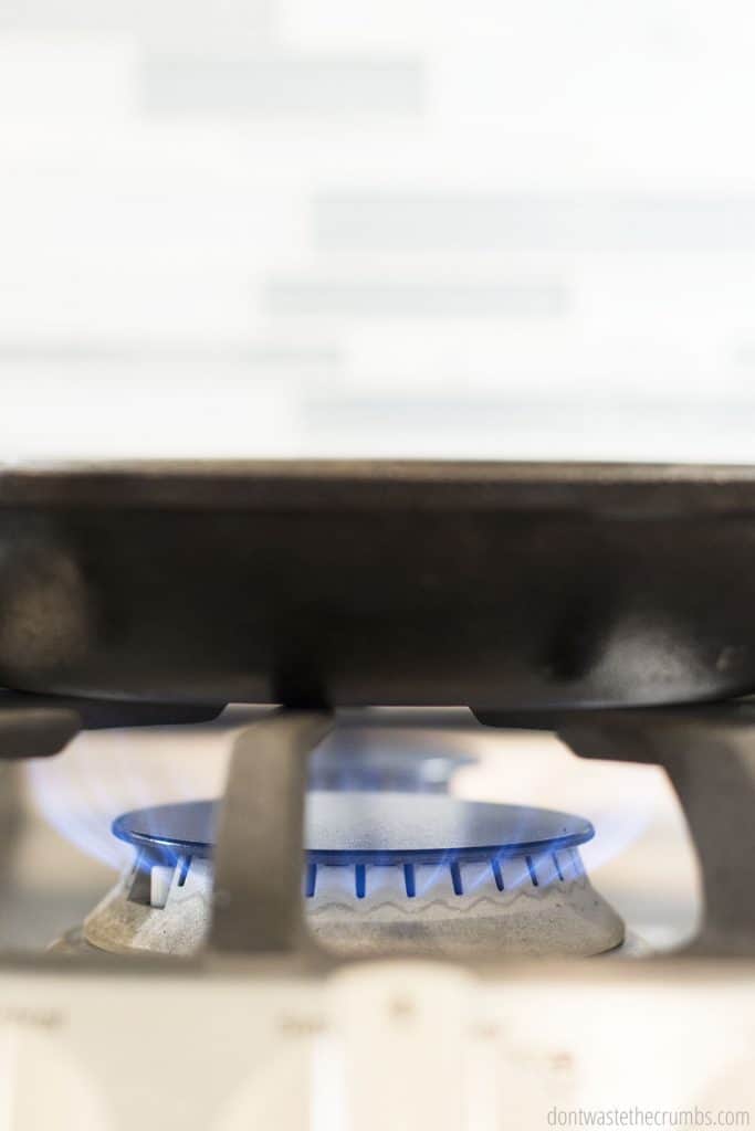 A cast iron skillet being dried over the stove with the burner on. 